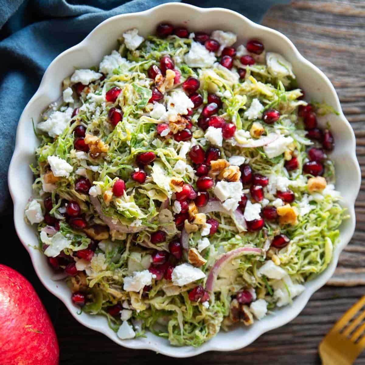 Shaved brussels sprout salad in a bowl topped with walnuts and pomegranate.