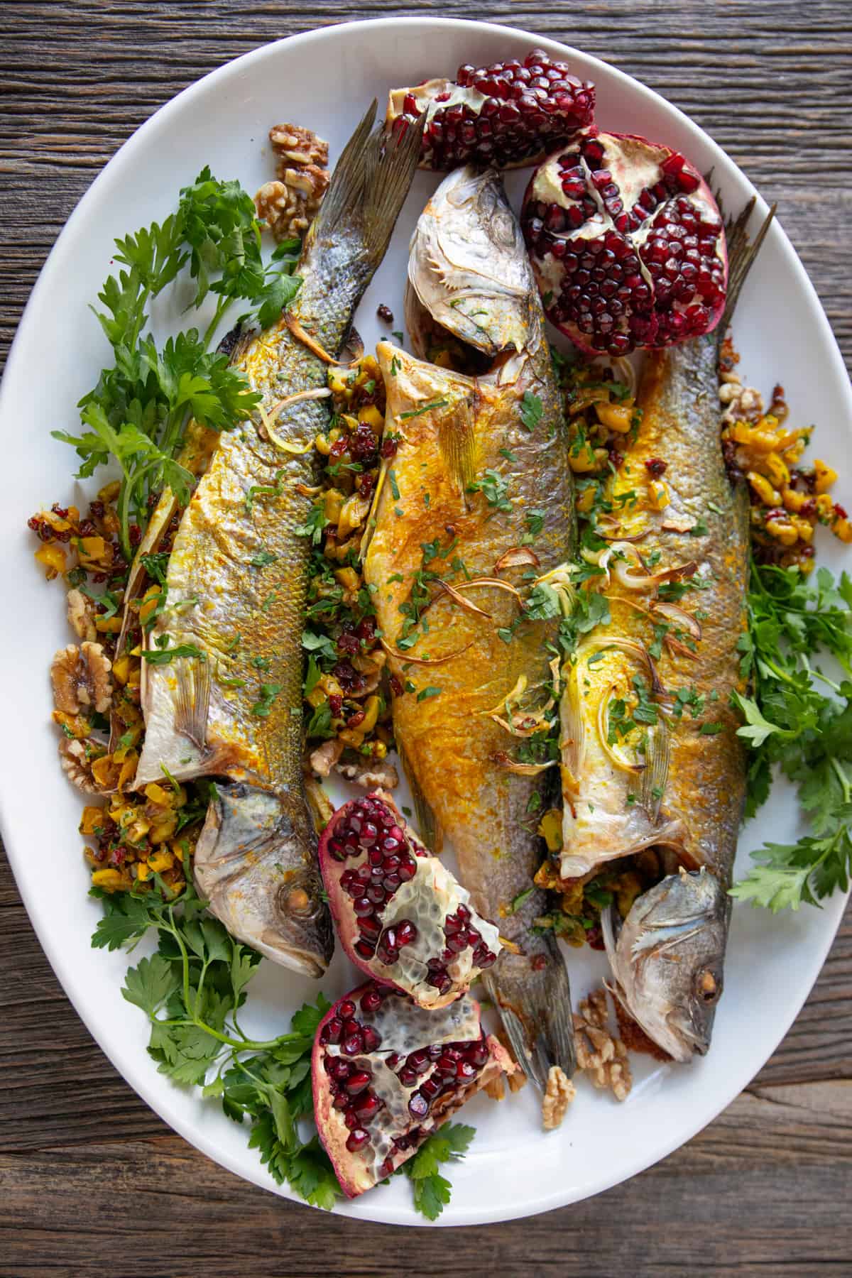 3 stuffed branzino on a platter with herbs and pomegranate. 