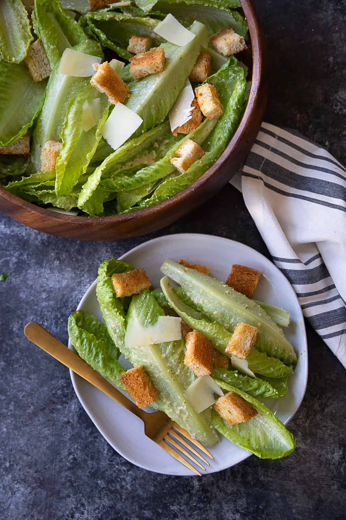 Caesar salad served on a white dish with a bowl of salad in the background