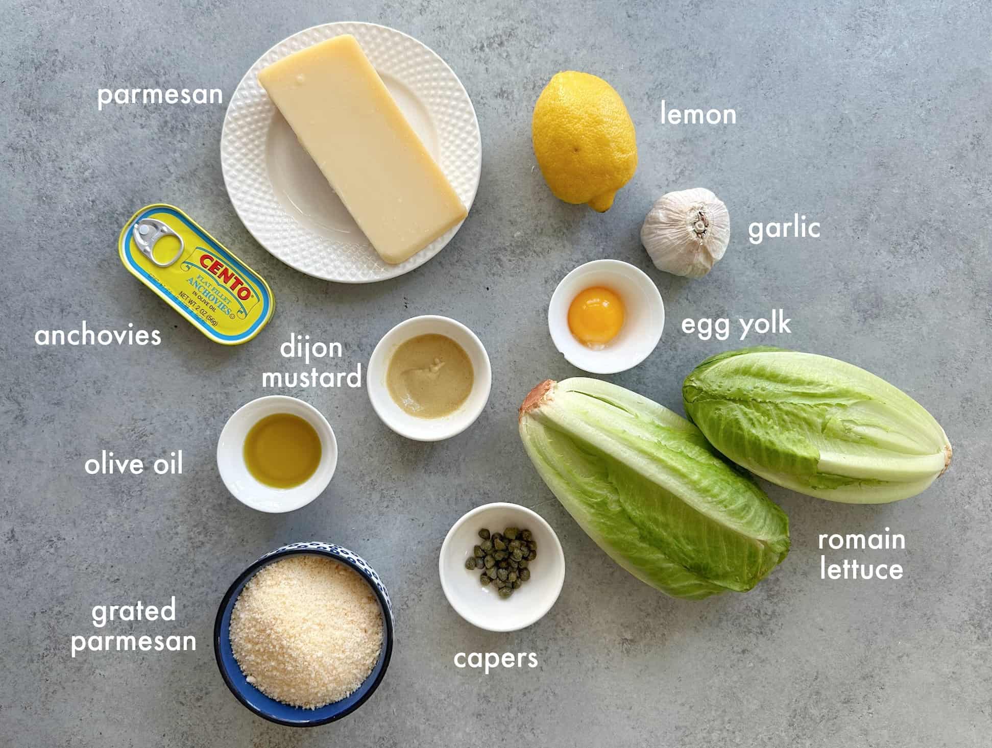 ingredients for Caesar salad: romaine lettuce, parmesan cheese, Dijon mustard, capers, anchovies, olive oil, garlic, egg yolk, and lemon