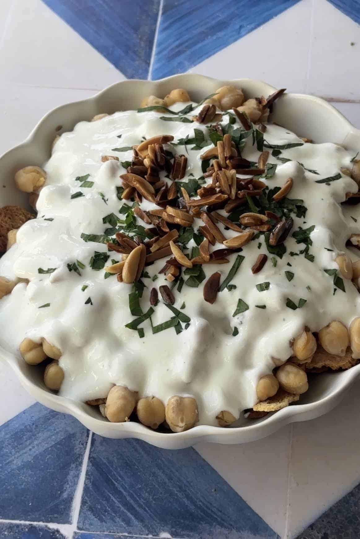 fatteh dish made with crispy pita, spiced chickpeas, creamy yogurt sauce and topped with slivered pine nuts and fresh parsley