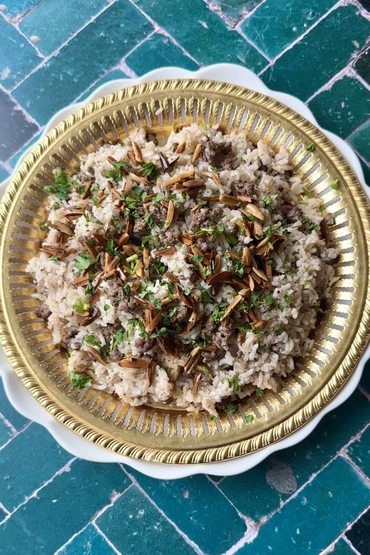 A close-up image of a plate filled with Hashweh rice, a Middle Eastern dish made with seasoned ground beef, rice, and aromatic spices, garnished with toasted almonds and fresh parsley.