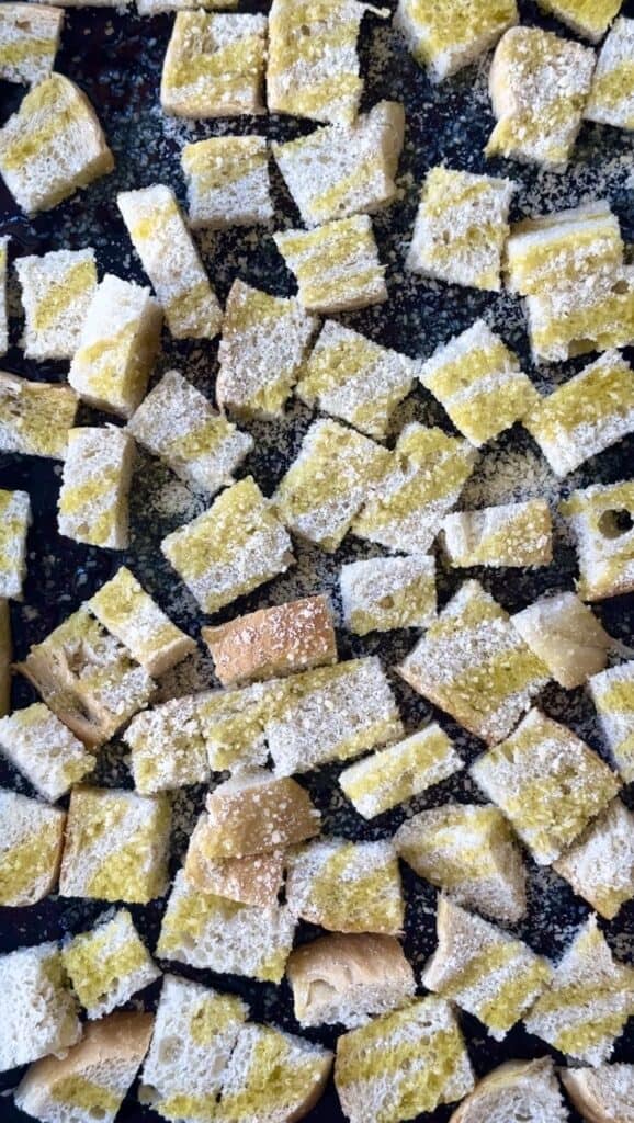 adding seasoning and olive oil to bread for croutons