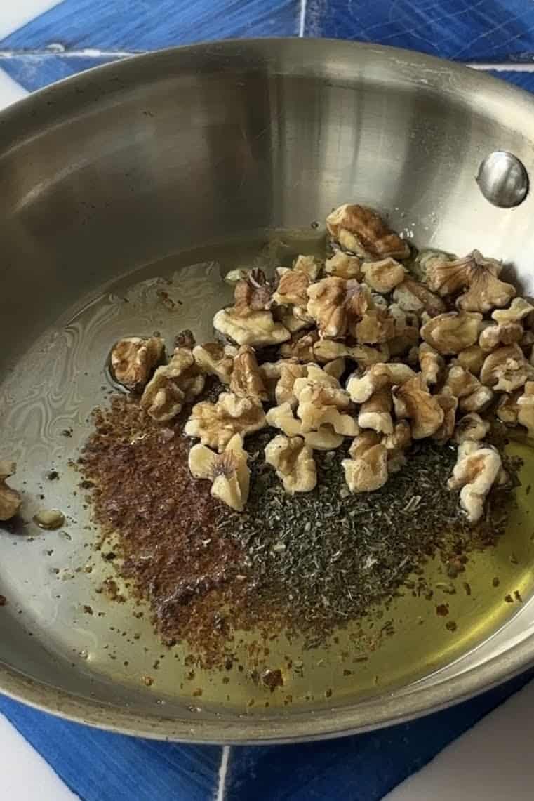 Olive oil in a pan with dried mint, Aleppo pepper and walnuts.
