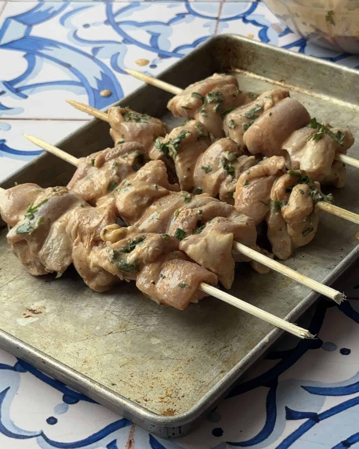 Four  Mediterranean chicken skewers threaded onto wooden skewers, ready for grilling.