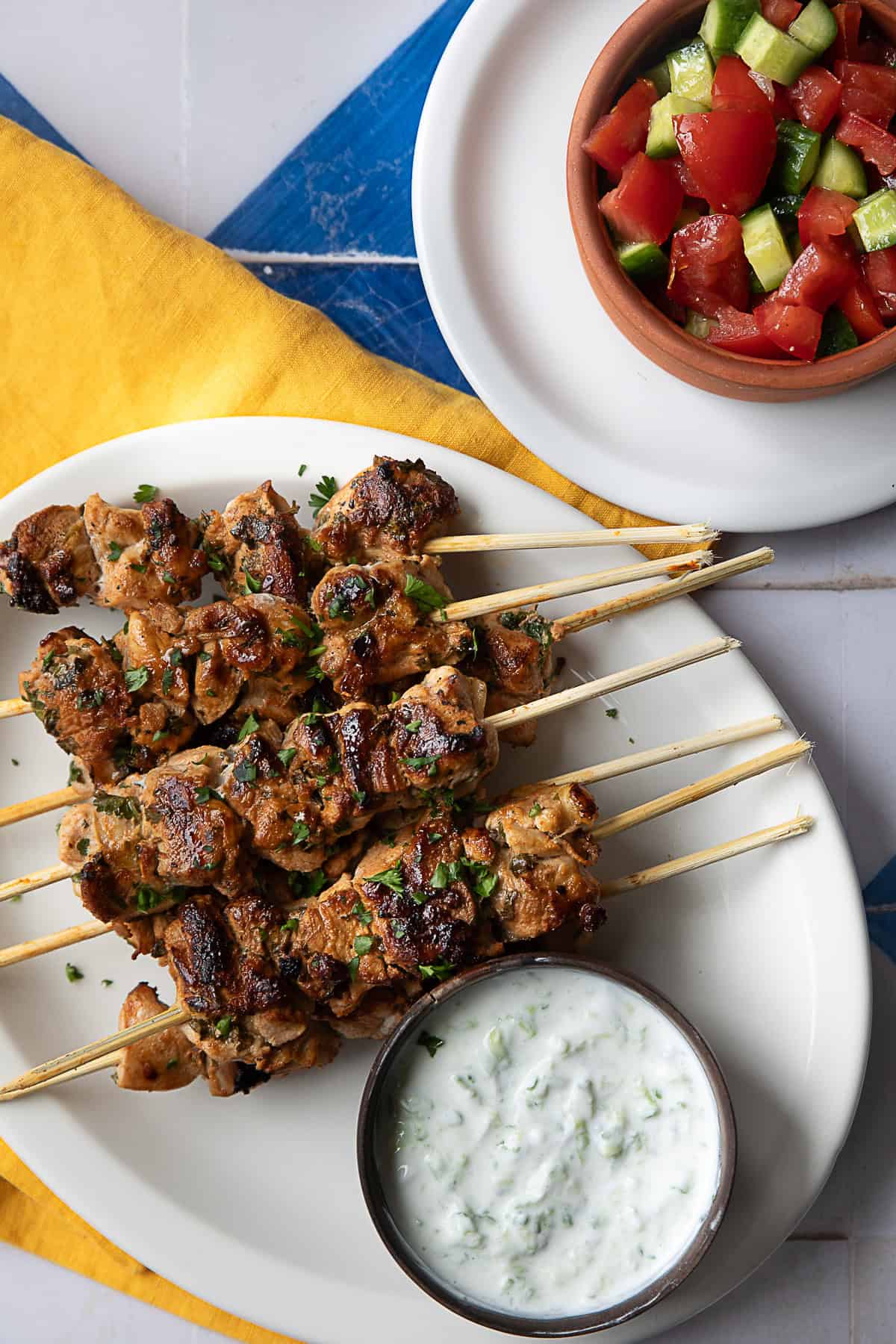 Golden-brown grilled Mediterranean chicken skewers arranged on a white plate, garnished with fresh herbs.