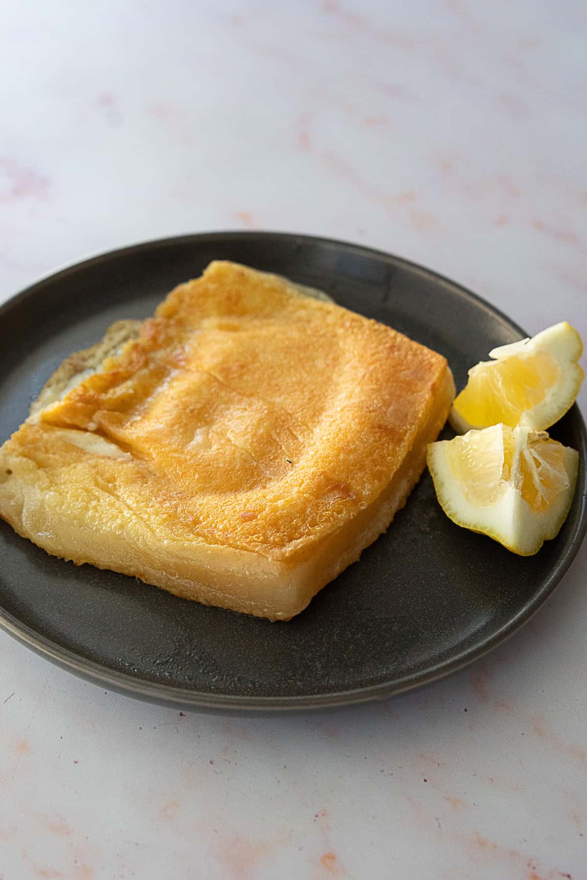 Golden brown Greek saganaki with two slices of lemon on the side.