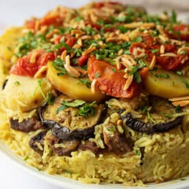 Maqluba dish, showcasing succulent meat, aromatic rice, and assorted vegetables, elegantly garnished with parsley and crunchy slivered almonds.