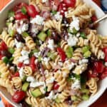 Greek pasta salad ingredients: Fusilli pasta, ripe tomatoes, cucumbers, red onions, Kalamata olives, feta cheese, Greek dressing.