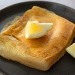 Saganaki fried cheese in a black plate topped with a slice of lemon.