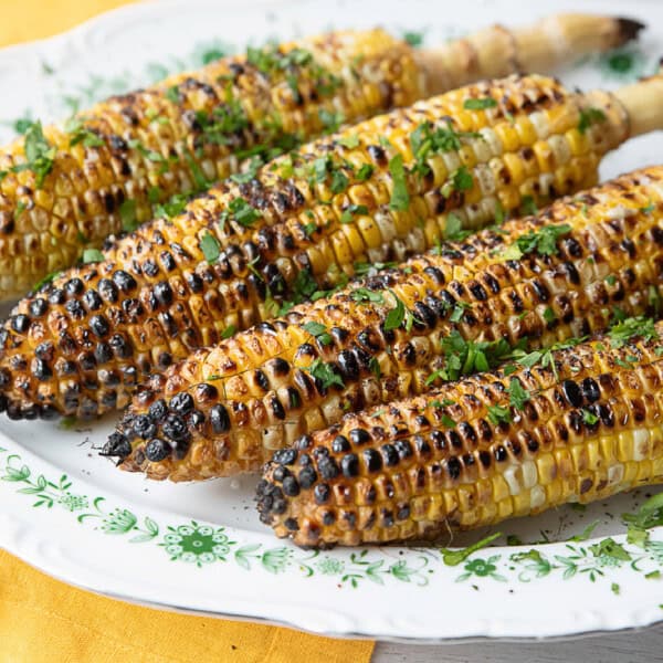 Close-up of grilled corn on the cob with char marks, seasoned with lemon juice, salt, sumac, and parsley. The golden kernels are perfectly cooked and juicy, making it an irresistible summer barbecue dish.
