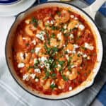 shrimp saganaki garnished with parsley and feta served in a white bowl with a blue brim