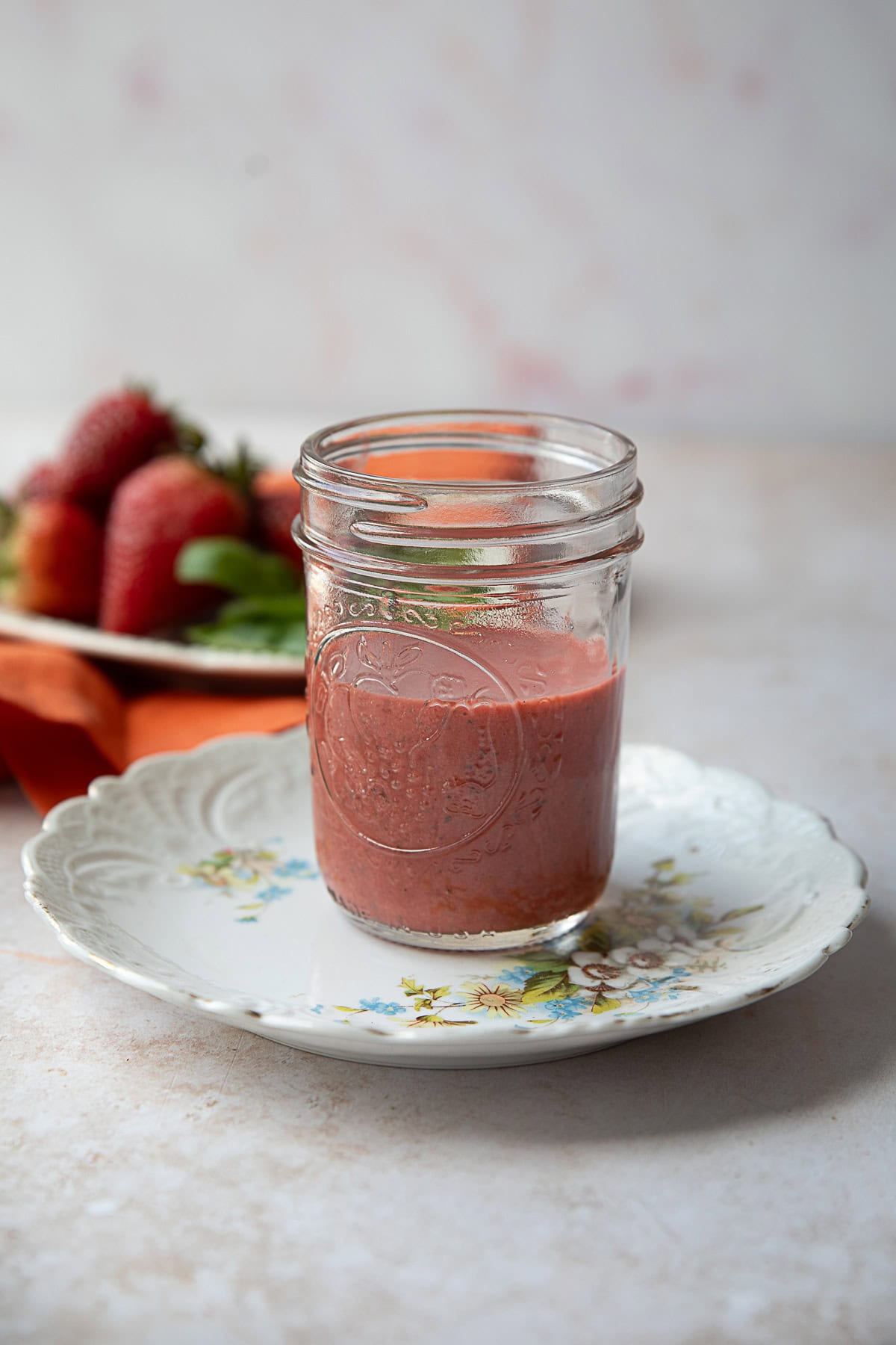 French Strawberry Vinaigrette strawberry vinaigrette in a glass jar on a white plate with strawberries in the background