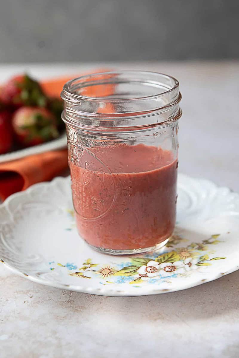 Best Strawberry Vinaigrette strawberry vinaigrette in a glass jar on a white plate with strawberries in the background