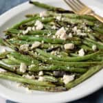 grilled green beans with lemon and feta served in a white dish with a fork next to them