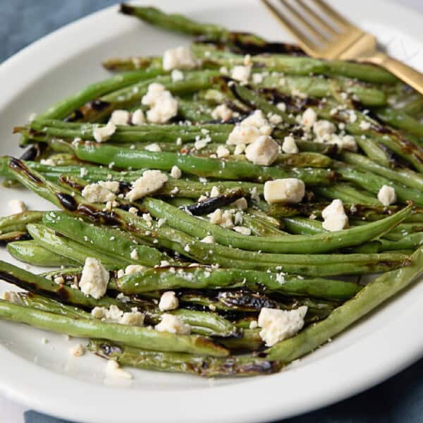 grilled green beans with lemon and feta served in a white dish with a fork next to them