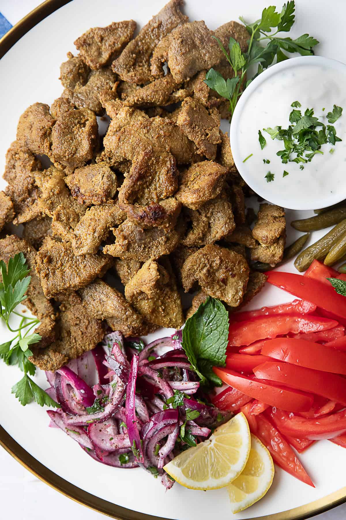 Easy Authentic Seared Lamb Shawarma easy authentic seared lamb shawarma served on a platter with shawarma sauce, sliced tomatoes, pickles, and red onions