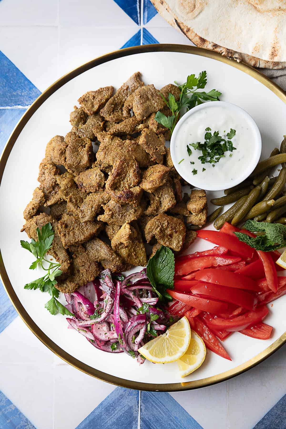 Easy Homemade Lamb Shawarma Recipe easy authentic seared lamb shawarma served on a platter with shawarma sauce, sliced tomatoes, pickles, and red onions