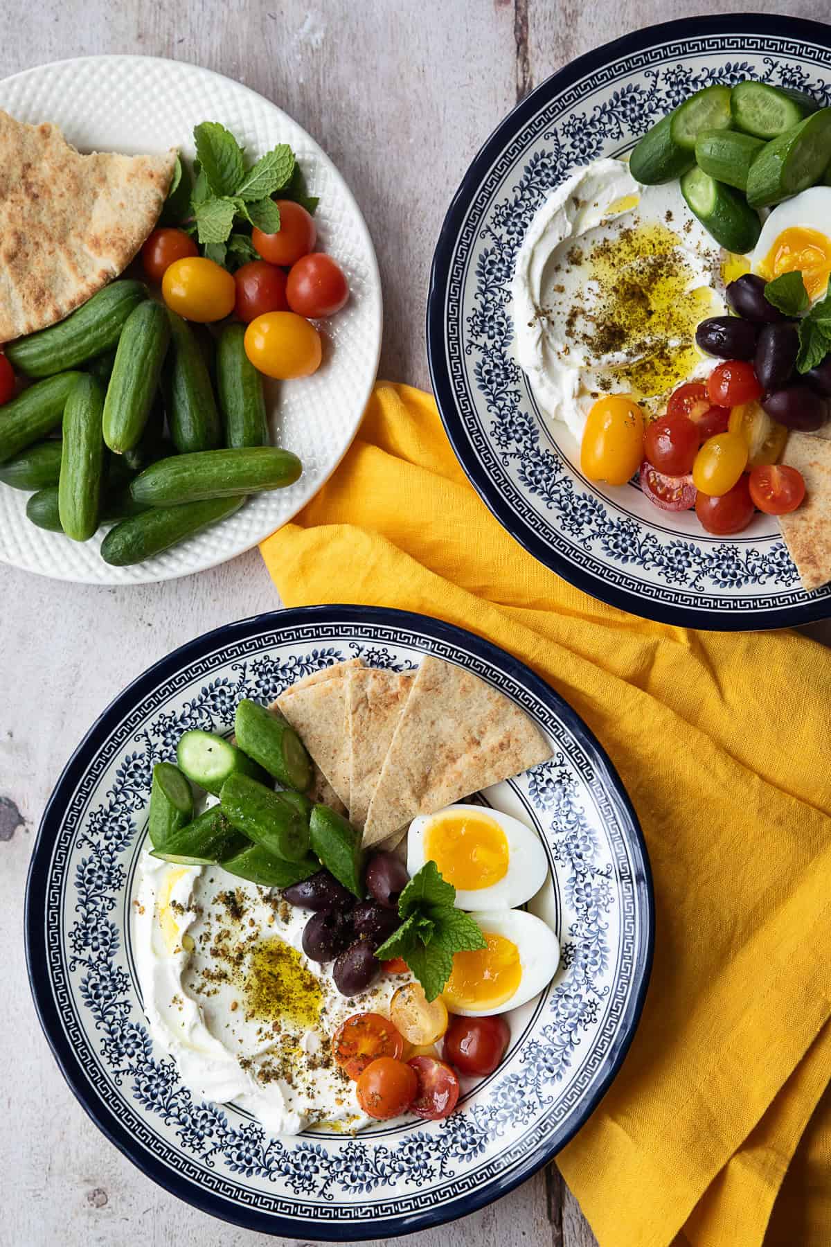 Two bowls with labneh and eggs and vegetables with a plate of vegetables.