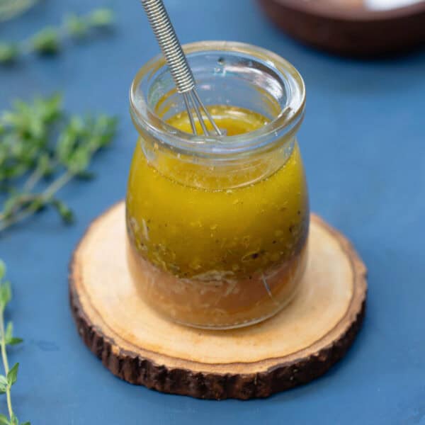 Greek vinaigrette salad dressing in a clear serving jar with whisk