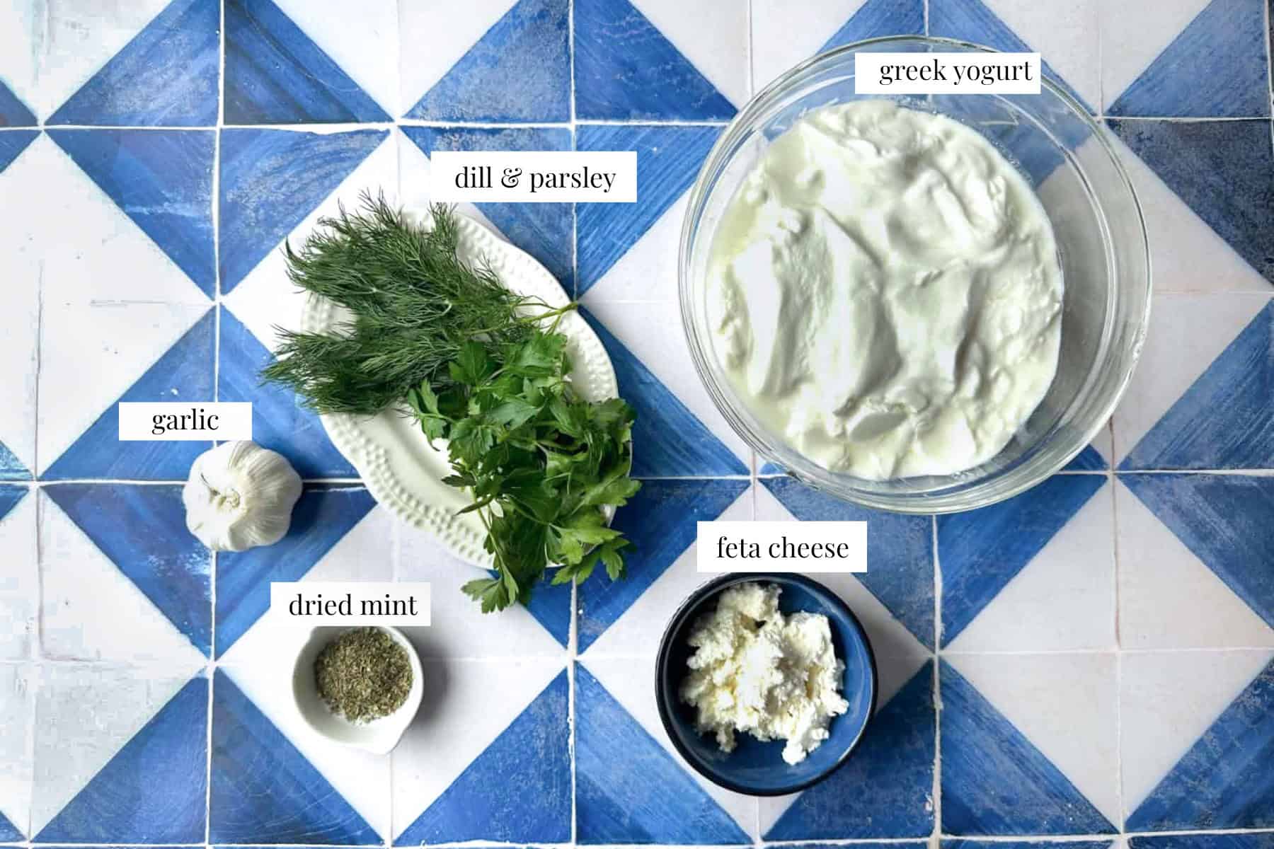 Haydari Ingredients An overhead shot of haydari ingredients: strained yogurt, feta cheese, garlic cloves, dried mint, and dill.