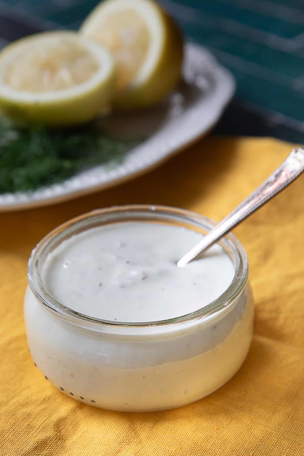 Tangy Feta Dressing a side view of a feta dressing glass jar placed next to a white plate of lemon halves and green herbs