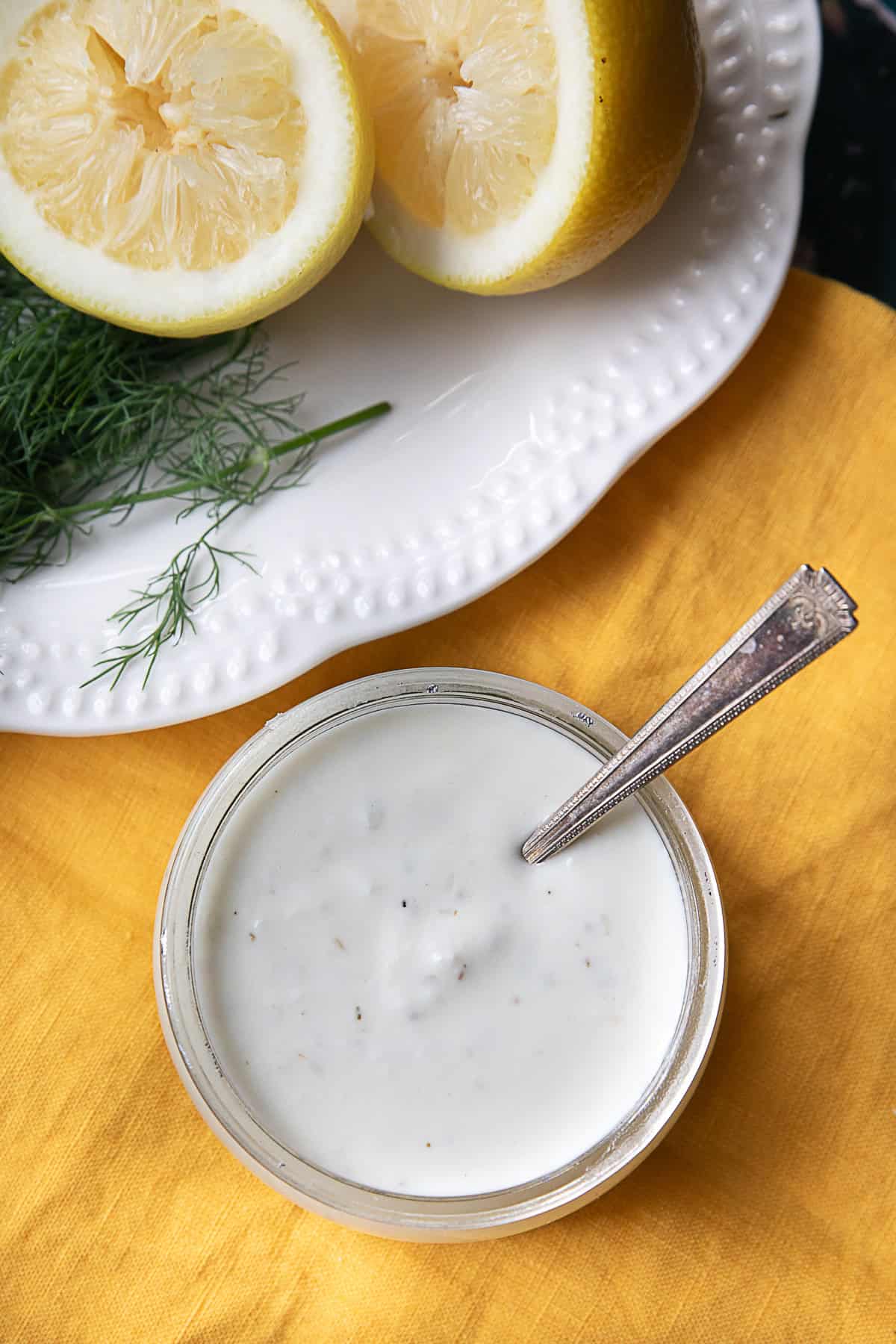 Feta Cheese Dressing a top view of a feta dressing glass jar placed next to a white plate of lemon halves and green herbs