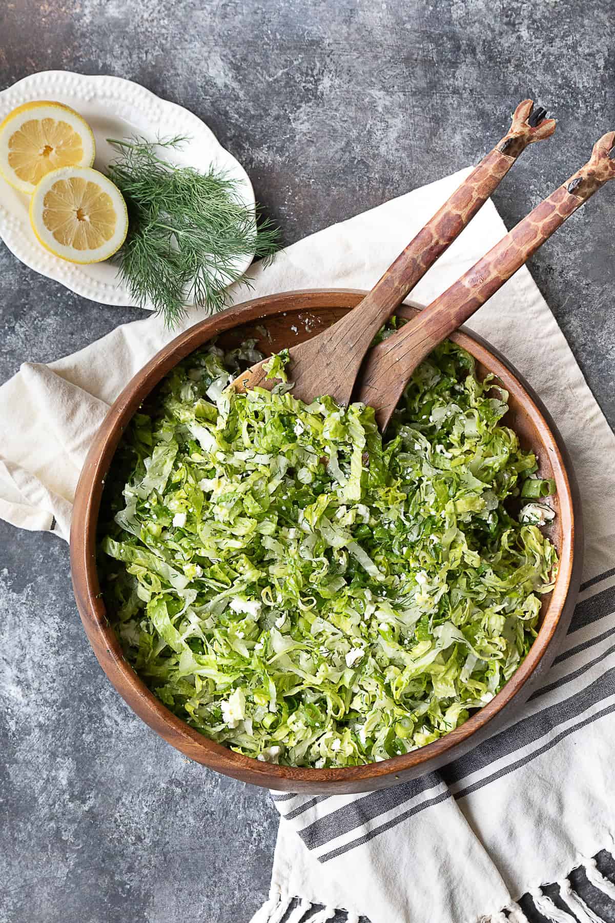 Fresh Greek Lettuce Salad A picture featuring a wooden bowl filled with Maroulosalata and a plate holding two lemon halves and some dill.