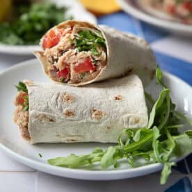 a close up view of two slices of Mediterranean tuna wraps served alongside of arugula leaves