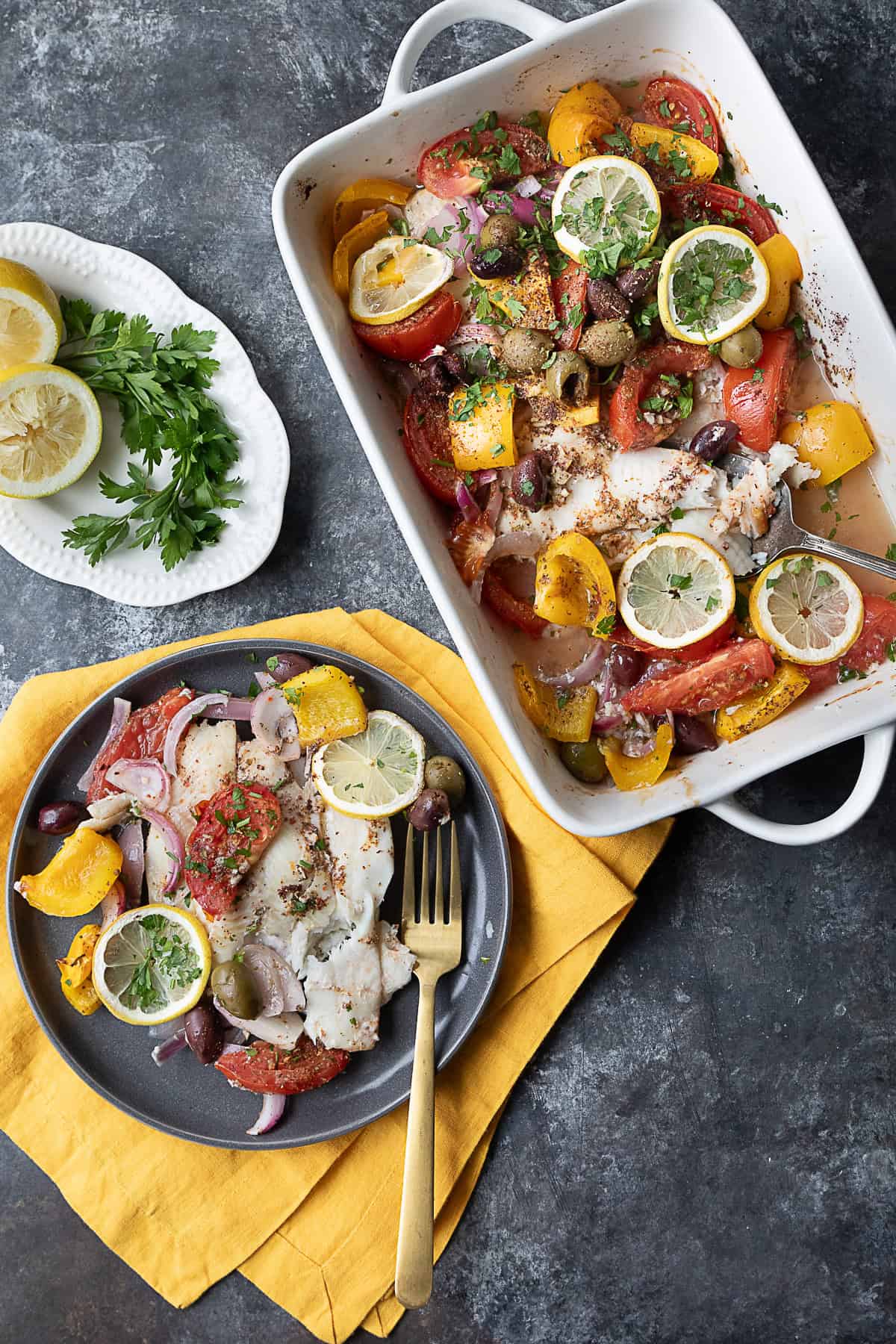 Mediterranean Baked Flounder Baked flounder surrounded by sliced bell peppers, tomatoes, red onions, and olives, topped with lemon slices and a blend of spices in a baking dish.