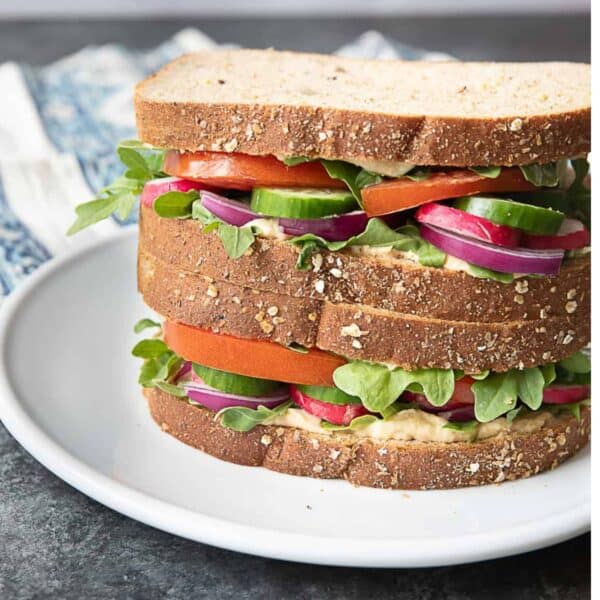 two hummus veggie sandwiches stacked on top of each other served on a white plate