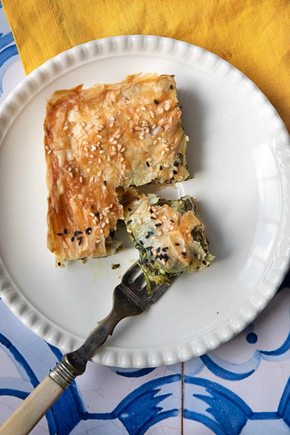 Spinach Borek Close-up of a serving of spinach borek on a plate, showing its crispy golden top and layers of filling, with a fork cutting into it.