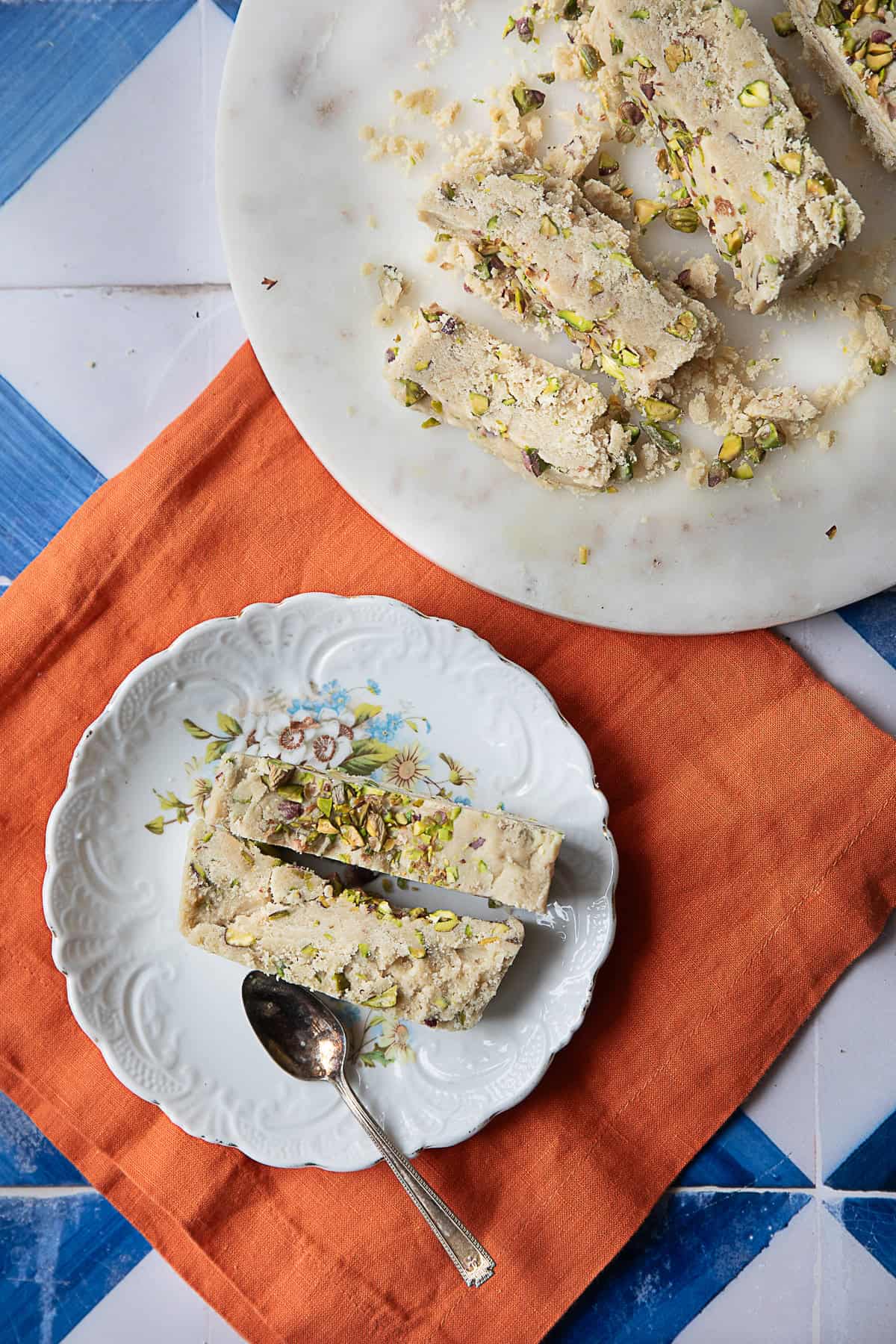 Best Tahini Halva (Halawa) Recipe tahini halva pieces served up in white plate with more tahini halva pieces in a larger serving plate in the background