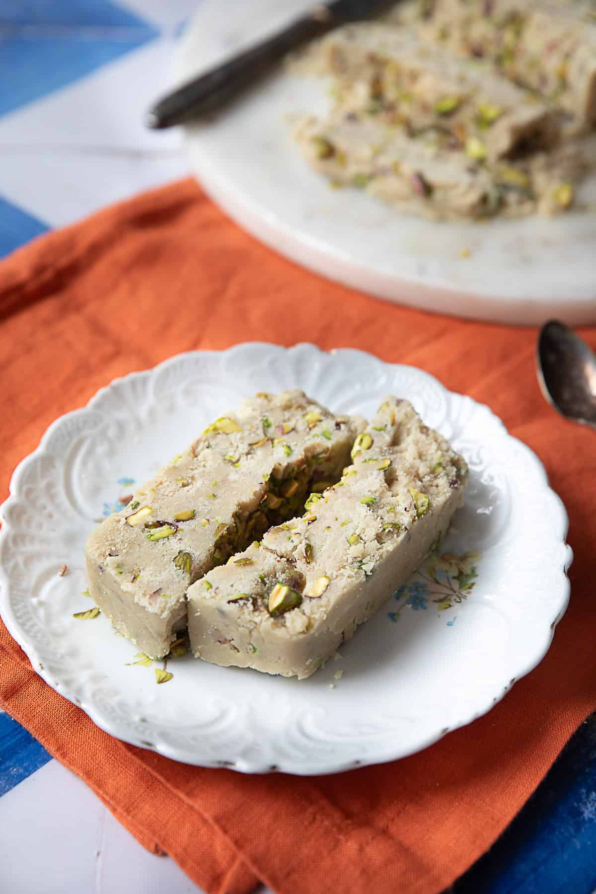 Tahini Halva Recipe tahini halva pieces served up in white plate with more tahini halva pieces in a larger serving plate in the background