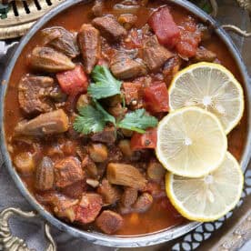 a bowl of bamya okra stew served hot with lemon wedges on top and a sprinkle of chopped parsley