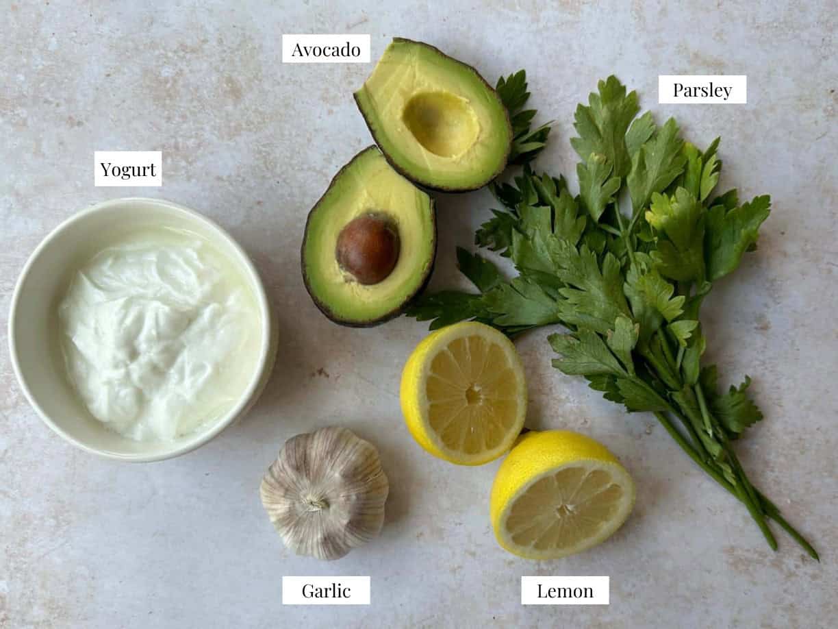 top view of ingredients of Greek yogurt avocado dressing: Greek yogurt, avocado, parsley, lemon, and garlic