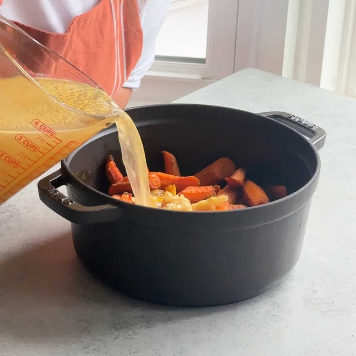 How to Make Roasted Carrot Soup add the vegetable broth to the roasted vegetables in the pot.