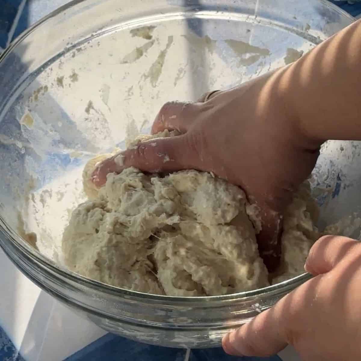 a woman combining ciabatta dough ingredients in a glass bowl