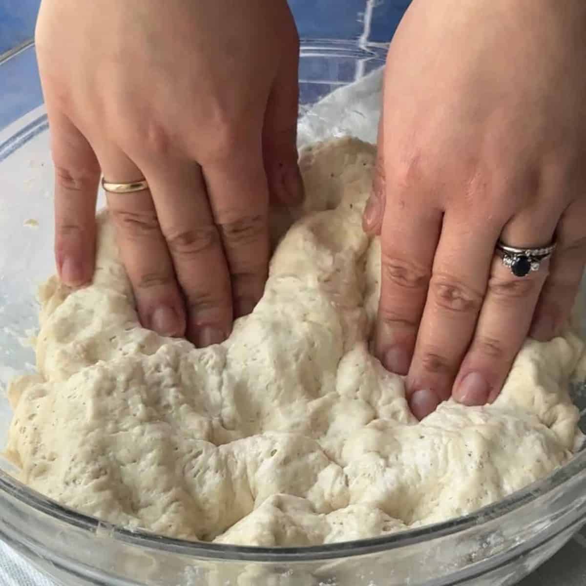 a woman pressing on the ciabatta dough with her fingers