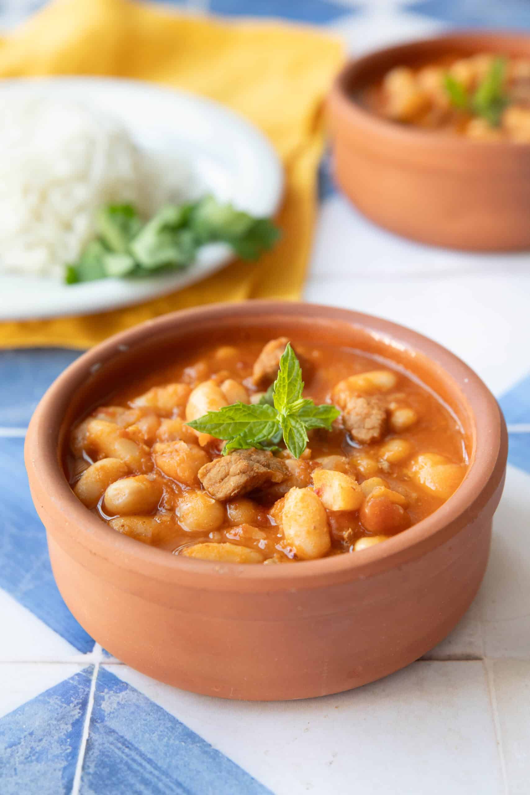 Turkish White Bean Stew Recipe Turkish white bean stew served in a small brown bowl with white rice in a dish in the background