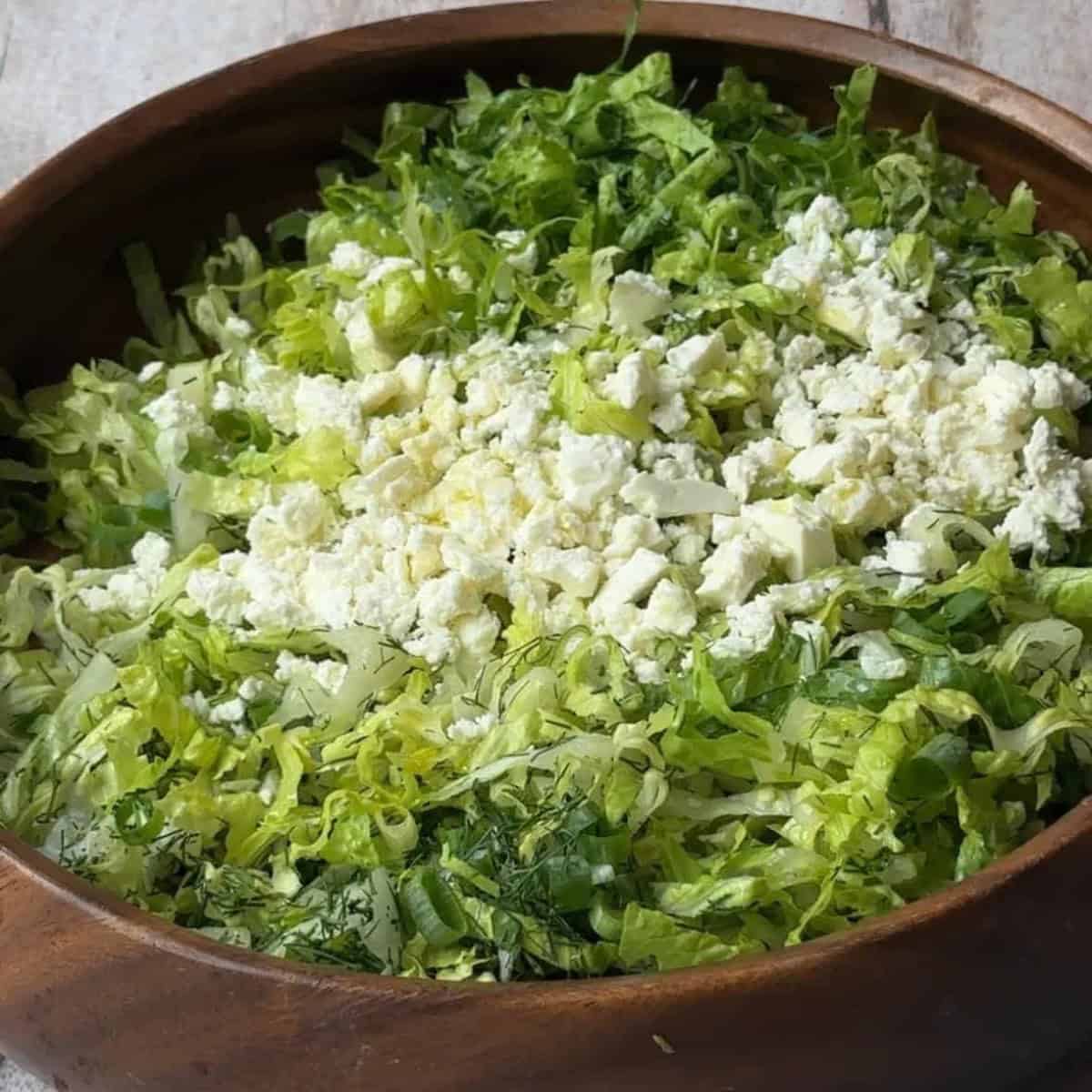 Classic Maroulosalata Recipe A large bowl of Maroulosalata featuring finely chopped lettuce, green onions, dill, and crumbled feta cheese.