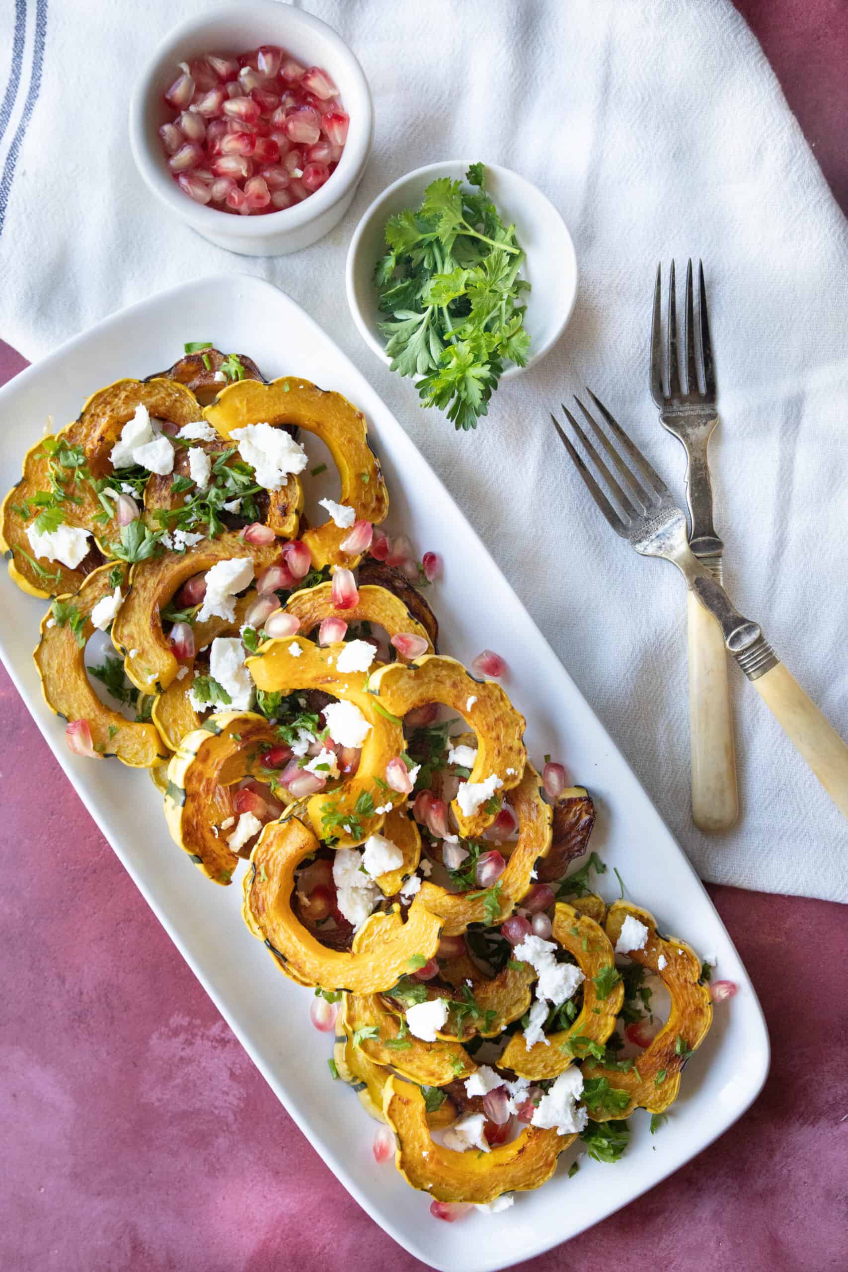 Easy Roasted Delicata Squash roasted delicata squash served on a white platter with feta and pomegranate seeds sprinkled on top with some parsley as garnish