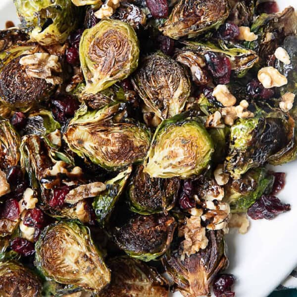 Golden roasted Brussels sprouts drizzled with tangy balsamic glaze, topped with crunchy walnuts and sweet dried cranberries, served on a white plate.