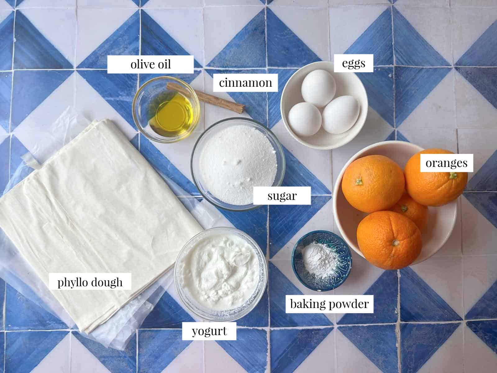 Greek Orange Cake Ingredients for Portokalopita laid out, including phyllo dough, eggs, fresh oranges, sugar, olive oil, Greek yogurt, baking powder, baking soda, and a cinnamon stick