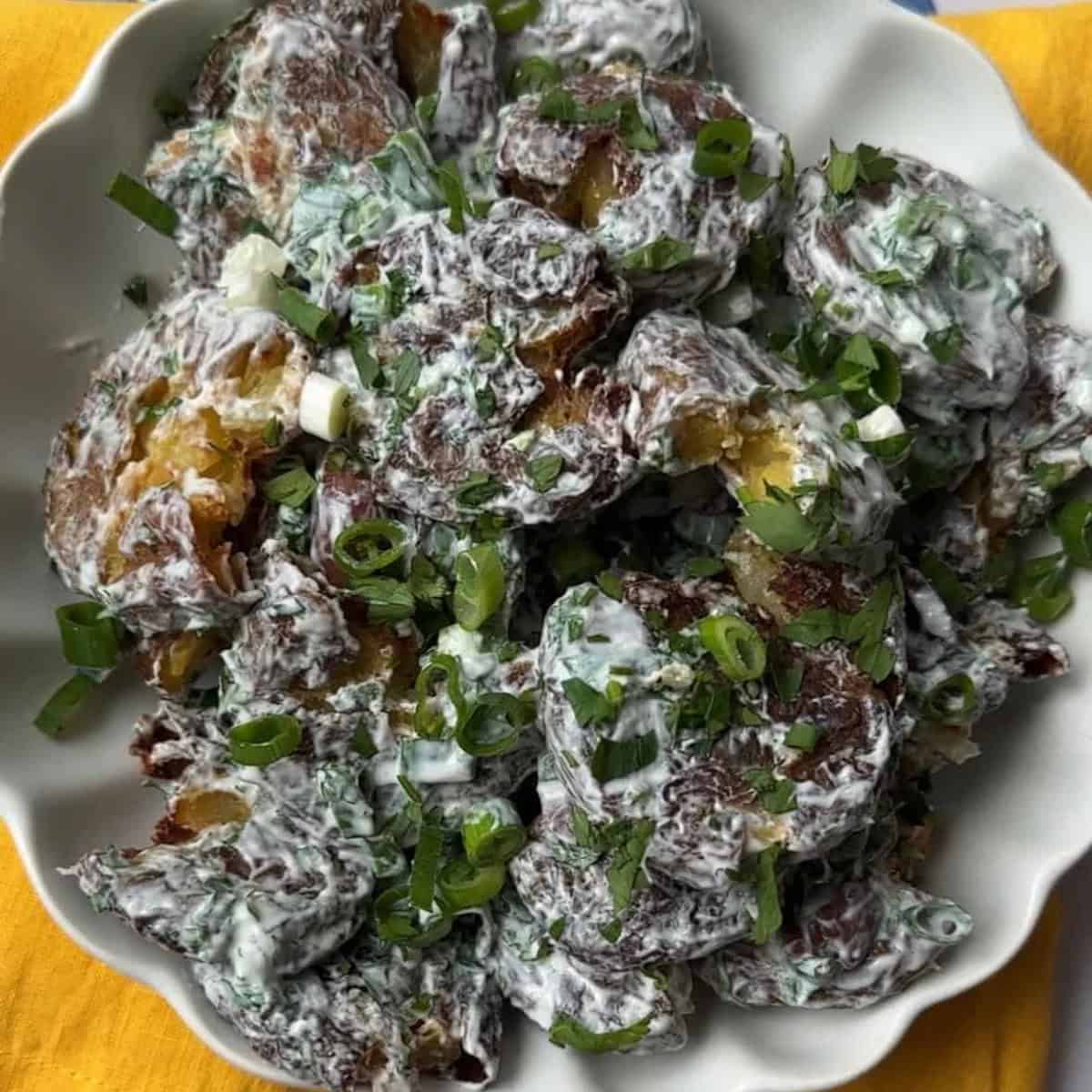 Smash Potato Salad with Dressing Smashed potato salad tossed in yogurt tahini dressing and garnished with fresh herbs