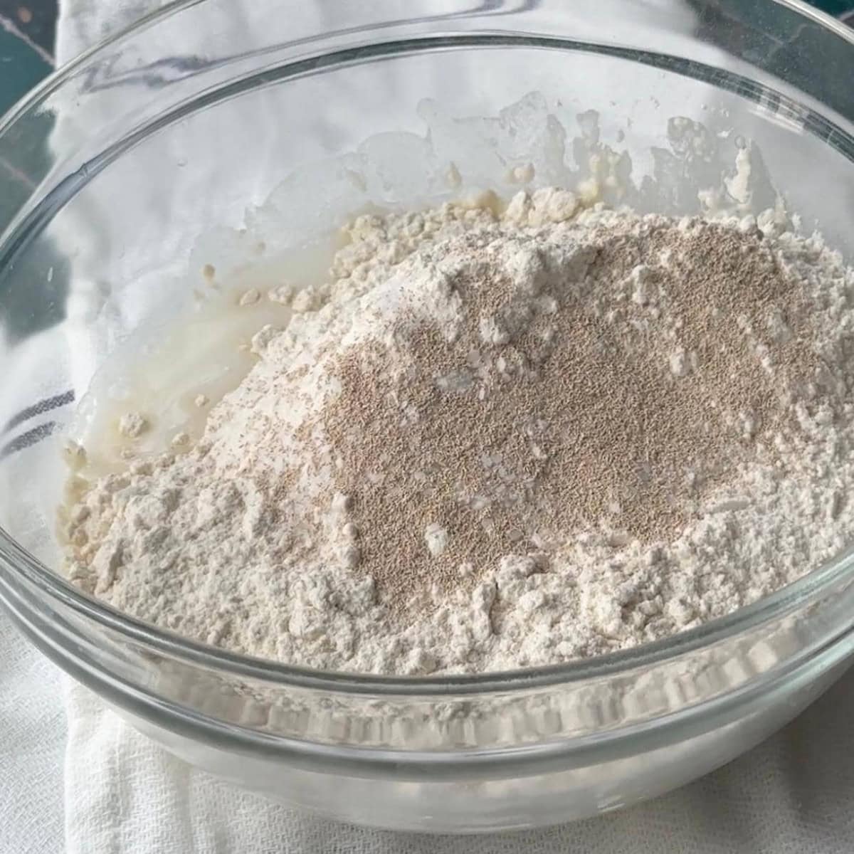 How To Make Pogaca Rolls A mixing bowl filled with a blend of flour, warm milk, warm water, instant yeast, sugar, and kosher salt.