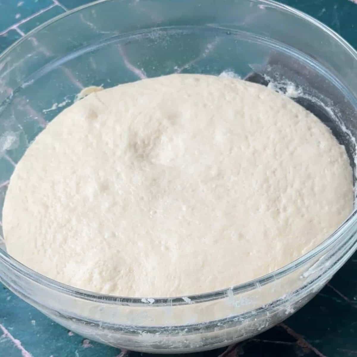 How To Make Pogaca Rolls A mixing bowl filled with a blend of flour, warm milk, warm water, instant yeast, sugar, and kosher salt, ready to be kneaded into a soft dough for making Pogaca