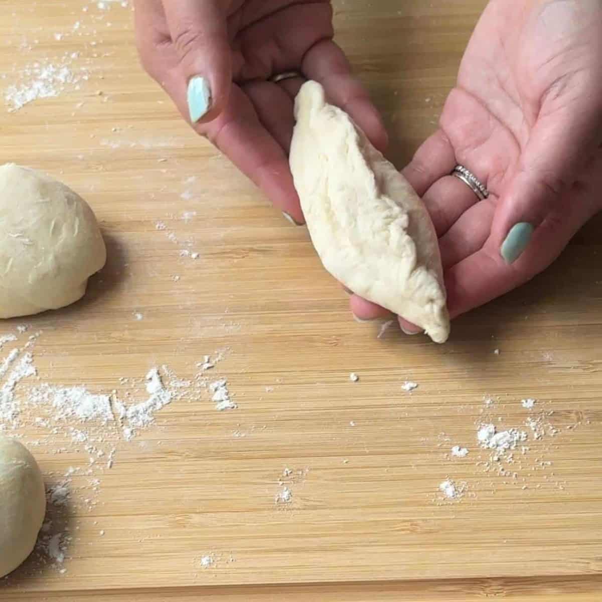 How To Make Pogaca Rolls A hand carefully shaping a piece of dough filled with feta and parsley, ready to be sealed into a crescent shape for baking Pogaca