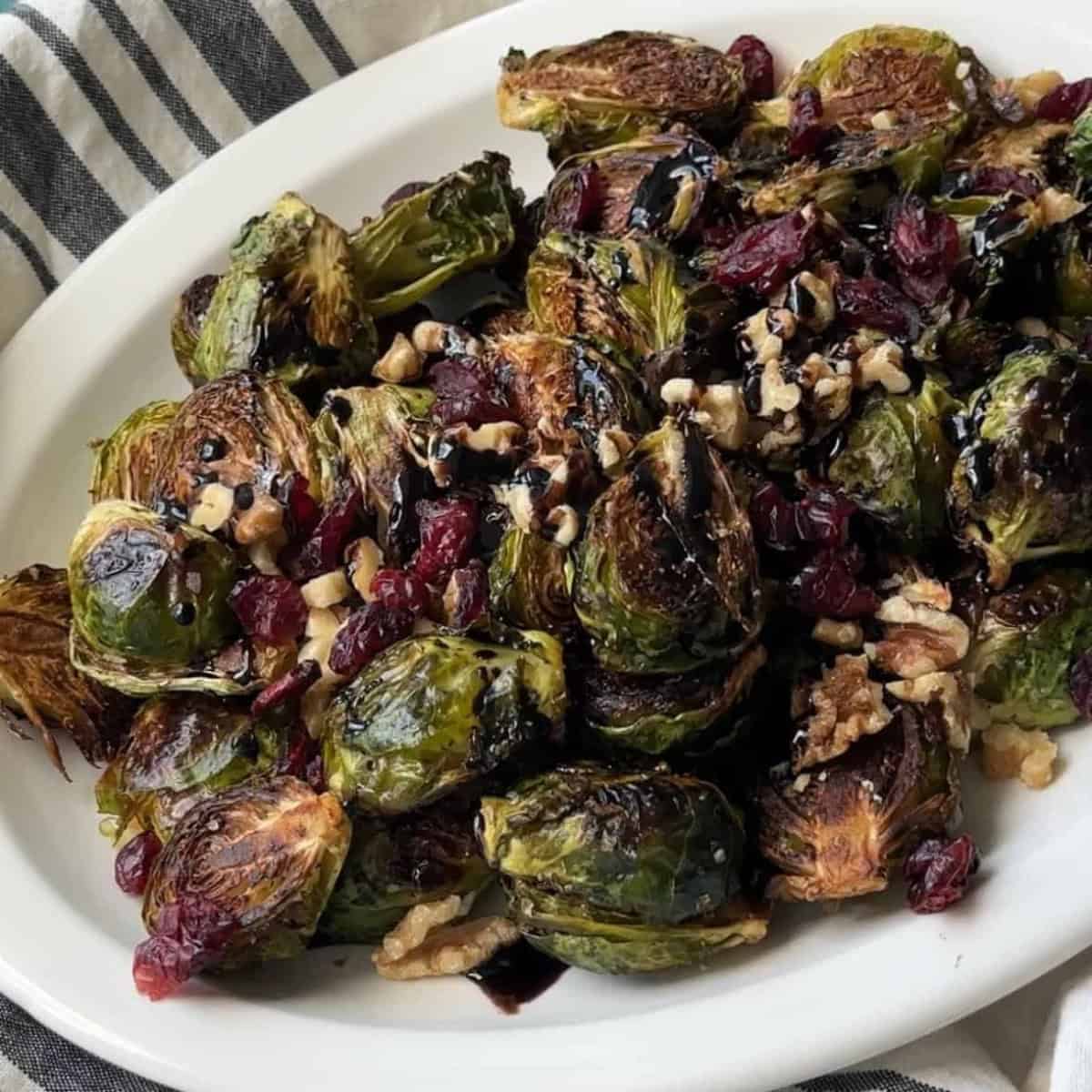 How To Make Balsamic-Glazed Brussels Sprouts Golden roasted Brussels sprouts topped with balsamic glaze, chopped walnuts, and dried cranberries on a serving plate