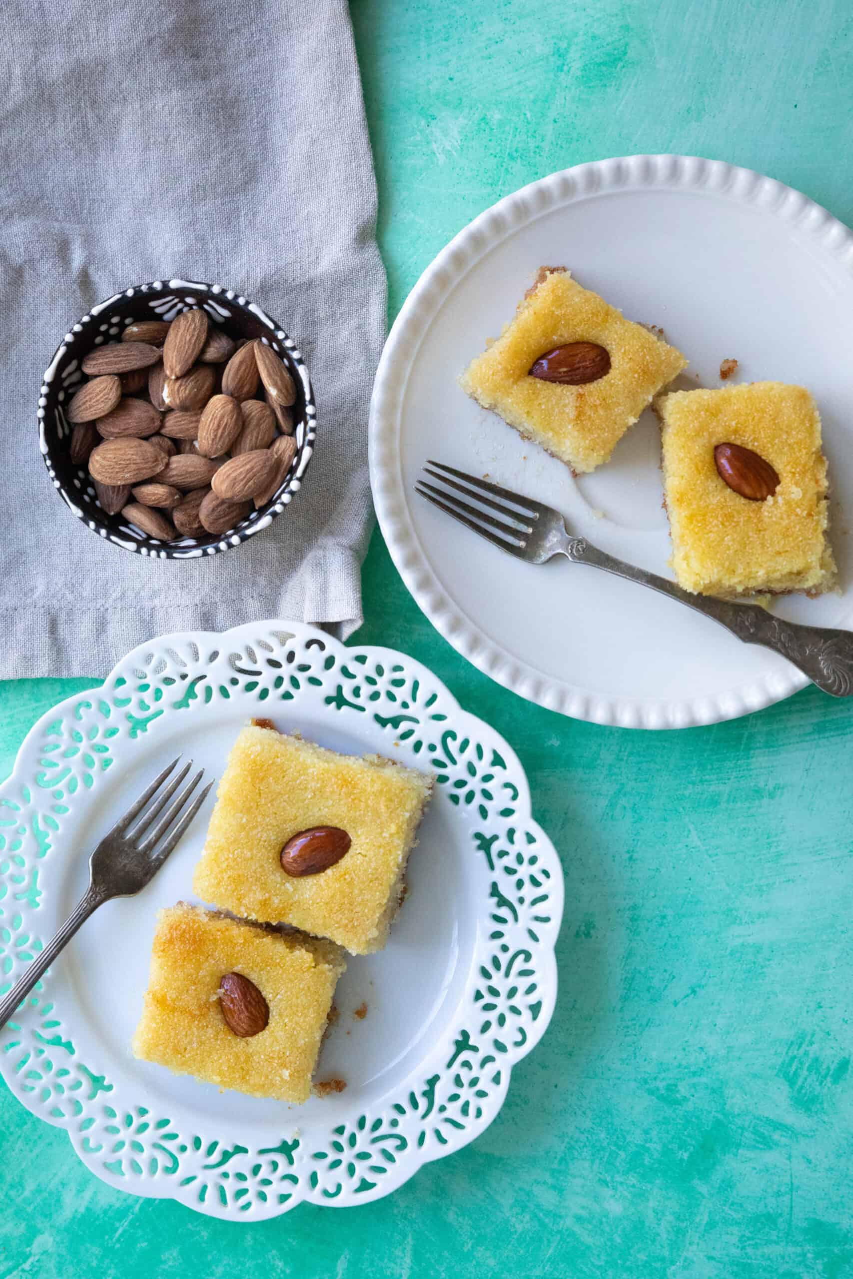Basbousa basbousa (semolina cake) presented every two pieces in a separate decorative serving dish with a small bowl of almonds on the side